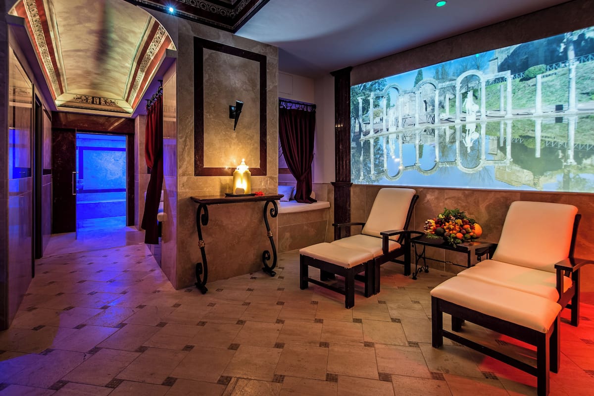 A spa area with two lounge chairs, a table with a candle, and a projection screen displaying a scenic view.