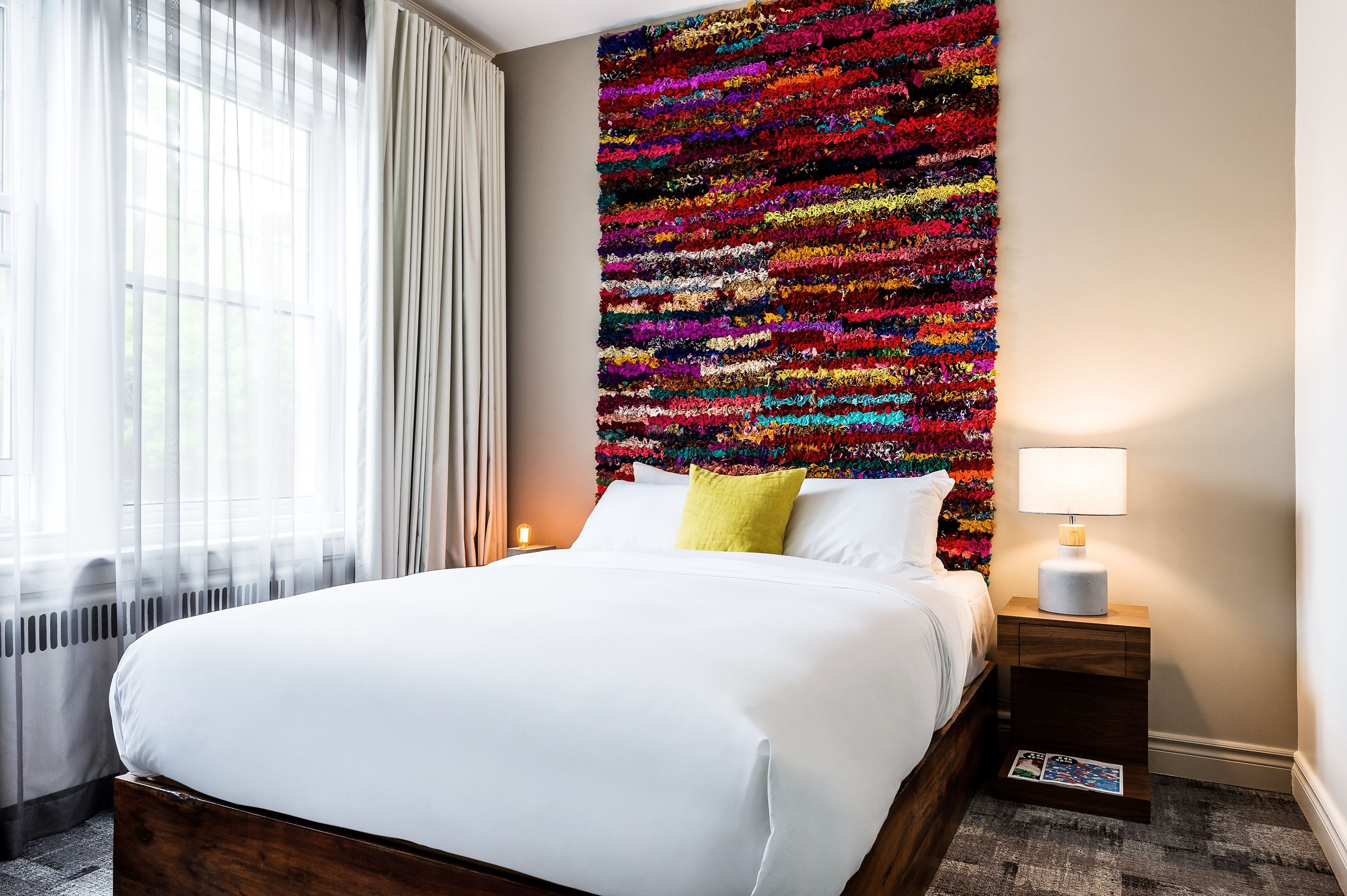 A hotel room with a large bed, a nightstand with a lamp, and a colorful wall art piece.