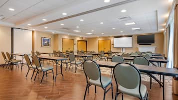 A conference room with multiple tables and chairs, a projector screen, and a television on the wall.