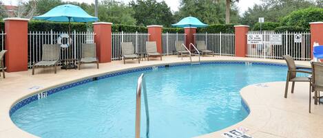 A swimming pool with a metal handrail, lounge chairs, and umbrellas.
