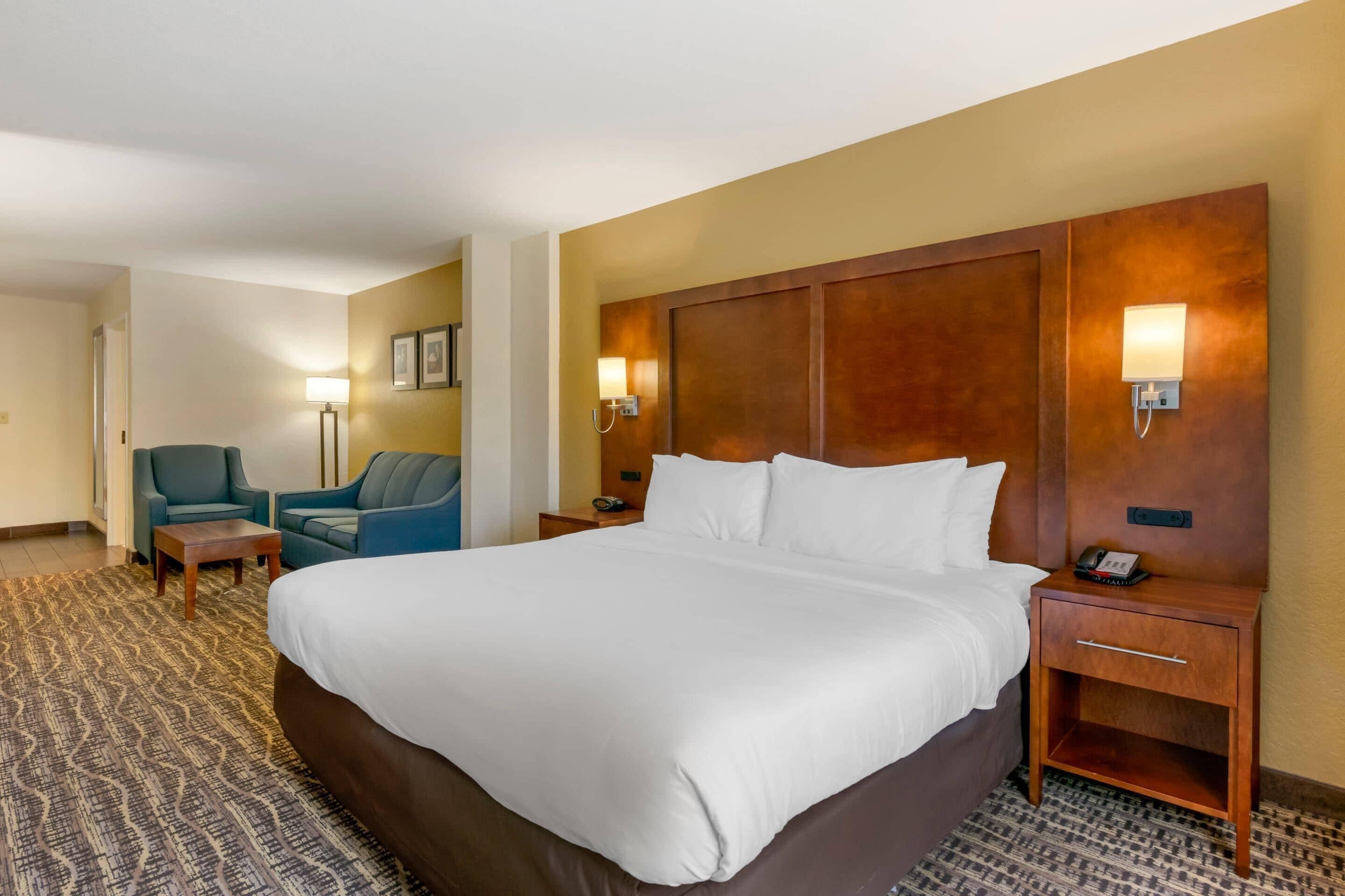 Een hotelkamer met een groot bed, een bureau, twee stoelen, een lamp en een nachtkastje met een telefoon.