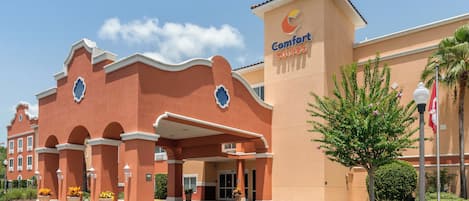 Un hôtel à la façade rouge, avec une enseigne indiquant « Comfort Suites » et une entrée abritée.