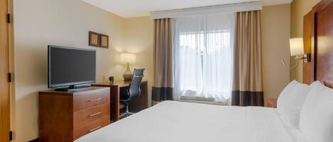 Une chambre d’hôtel avec un grand lit, un bureau avec une télévision, une chaise et une fenêtre avec des rideaux.