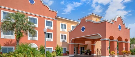 A multi-story hotel with a red facade, white trim, and a central entrance with a covered walkway.