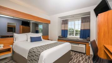 A hotel room with a bed, bedside table, TV, window with curtains, and a seating area by the window.