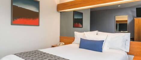 Habitación de hotel con una cama grande, una mesita de noche, un espejo y un cuadro en la pared.