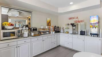 Una cocina moderna con armarios blancos, microondas, tostadora, cafetera y dispensador de jugo.