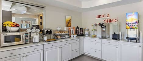 A modern kitchen with white cabinets, a microwave, toaster, coffee maker, and a juice dispenser.