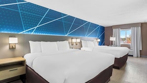 A hotel room with a large bed, two bedside tables, a nightstand, and a wall with a geometric pattern.