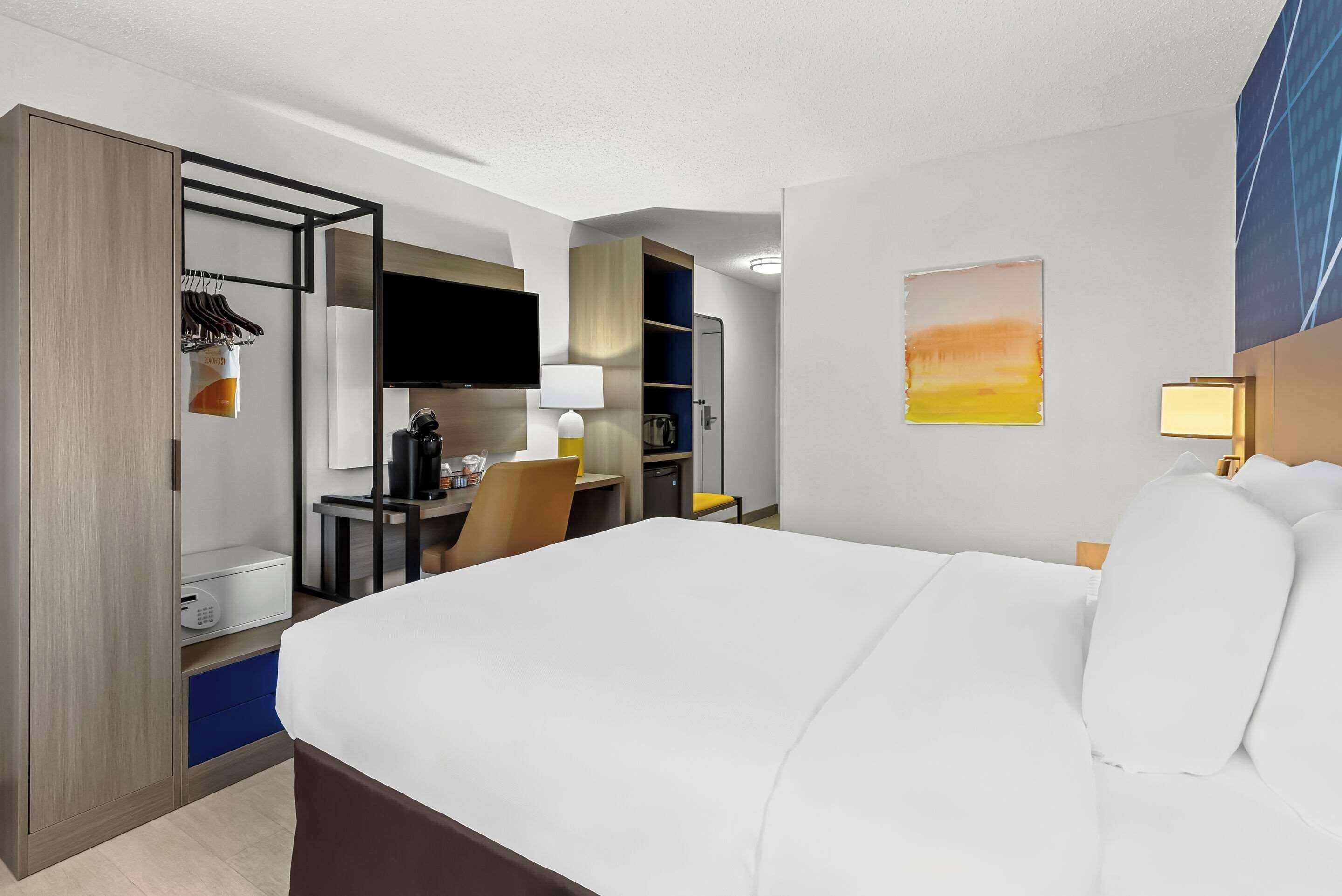 A hotel room with a bed, a desk, a chair, a TV, and a wardrobe.