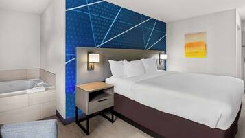 Una habitación de hotel moderna con una cama grande, una mesita de noche con lámpara, un pequeño rincón de descanso y una bañera.