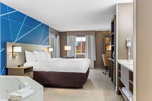 A hotel room with a large bed, a desk, a chair, a vanity with a mirror, and a window with curtains.