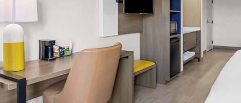 A hotel room with a desk, chair, television, and a small kitchenette.