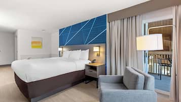 A hotel room with a large bed, a bedside table with a lamp, a chair, and a view of the outdoors.