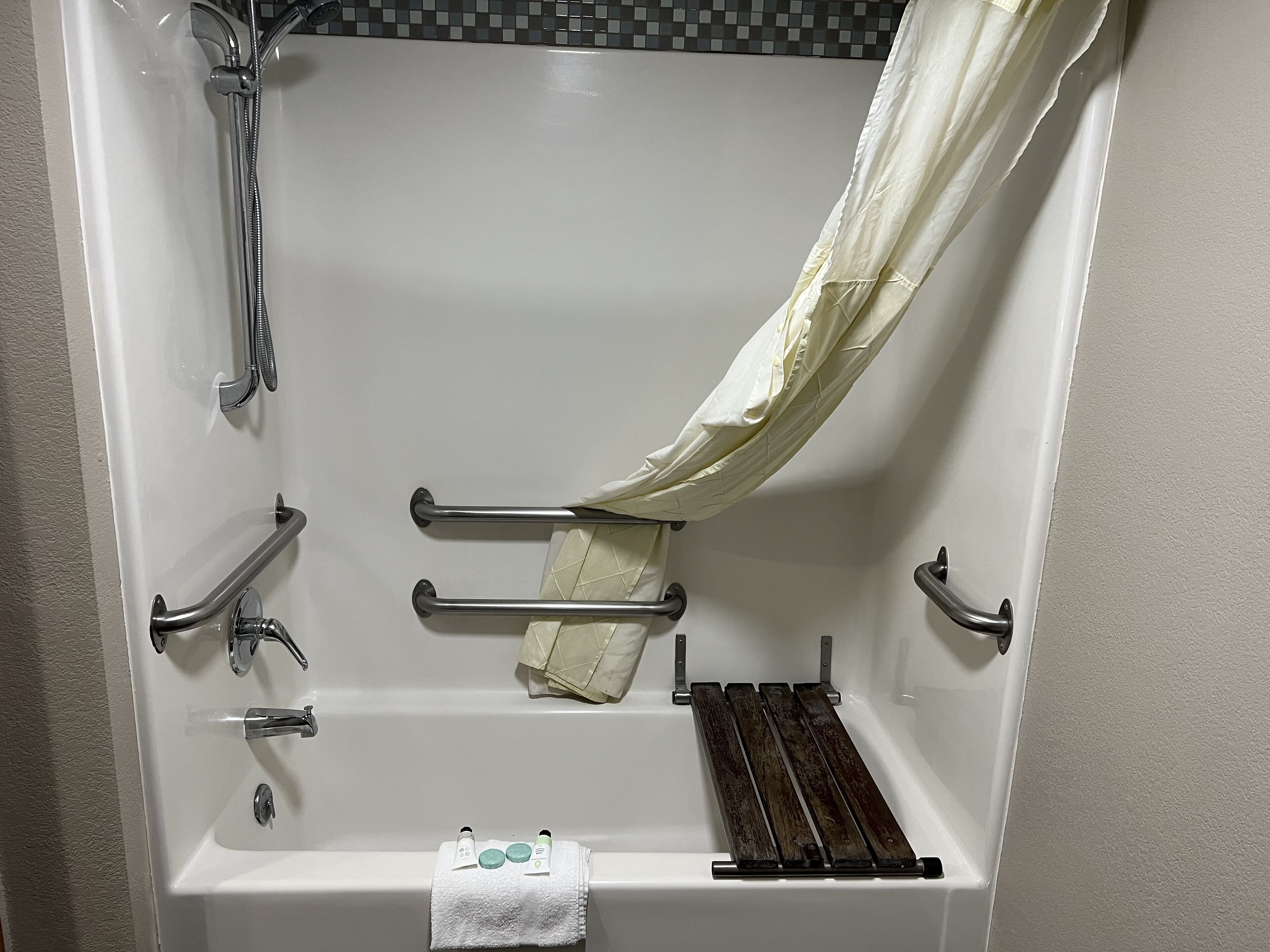 Bañera con cabezal de ducha, barras de apoyo y toallero.