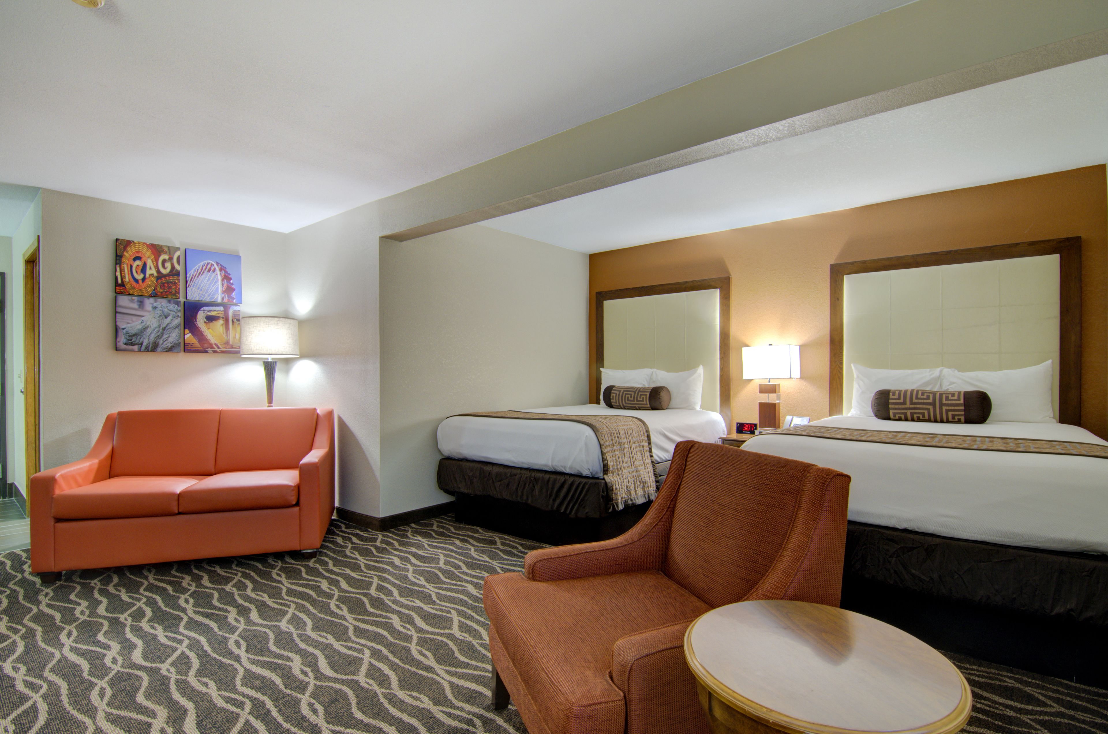 A hotel room with a bed, two chairs, a small table, and a patterned carpet.