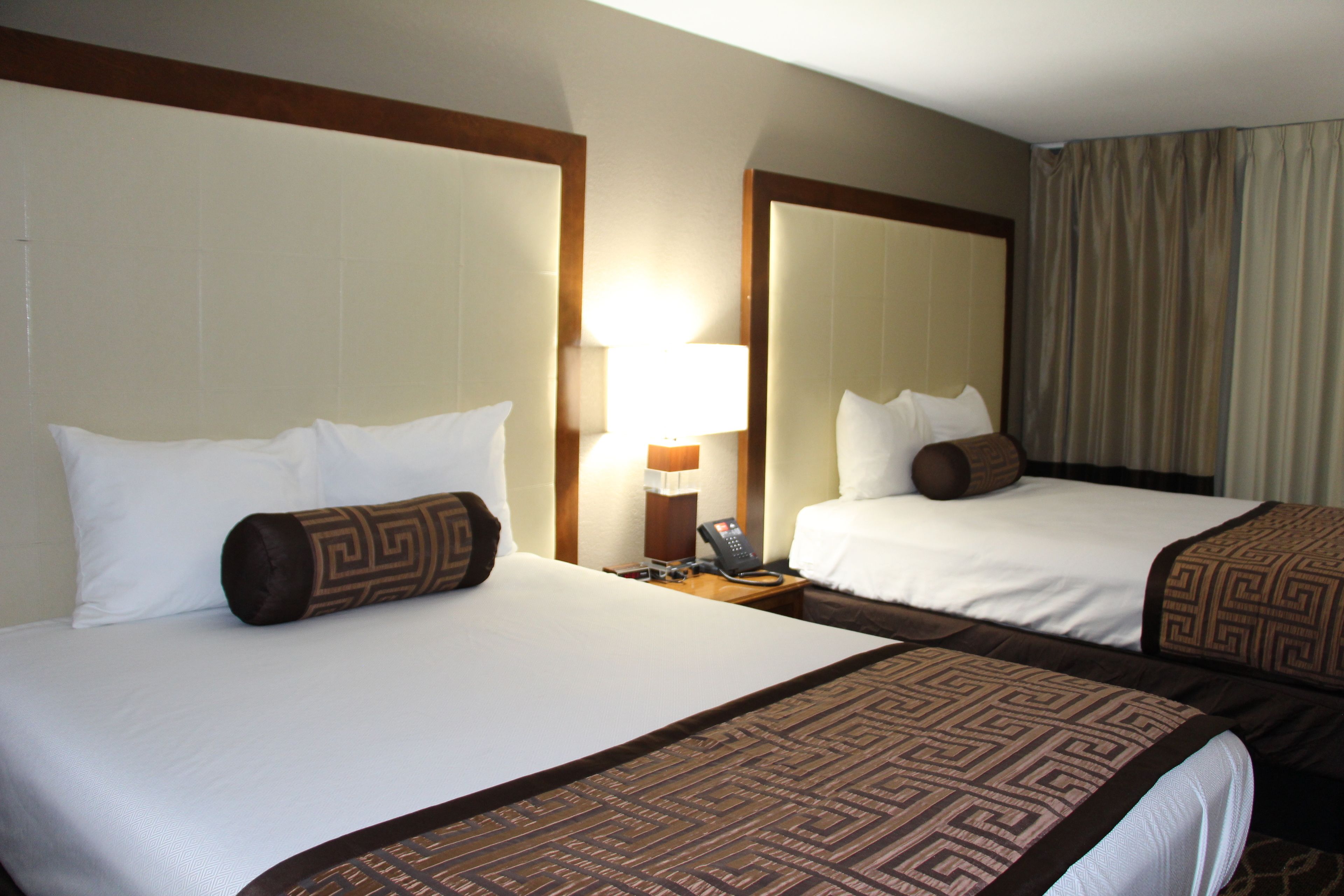 A hotel room with two beds, a nightstand with a lamp, and a large mirror.