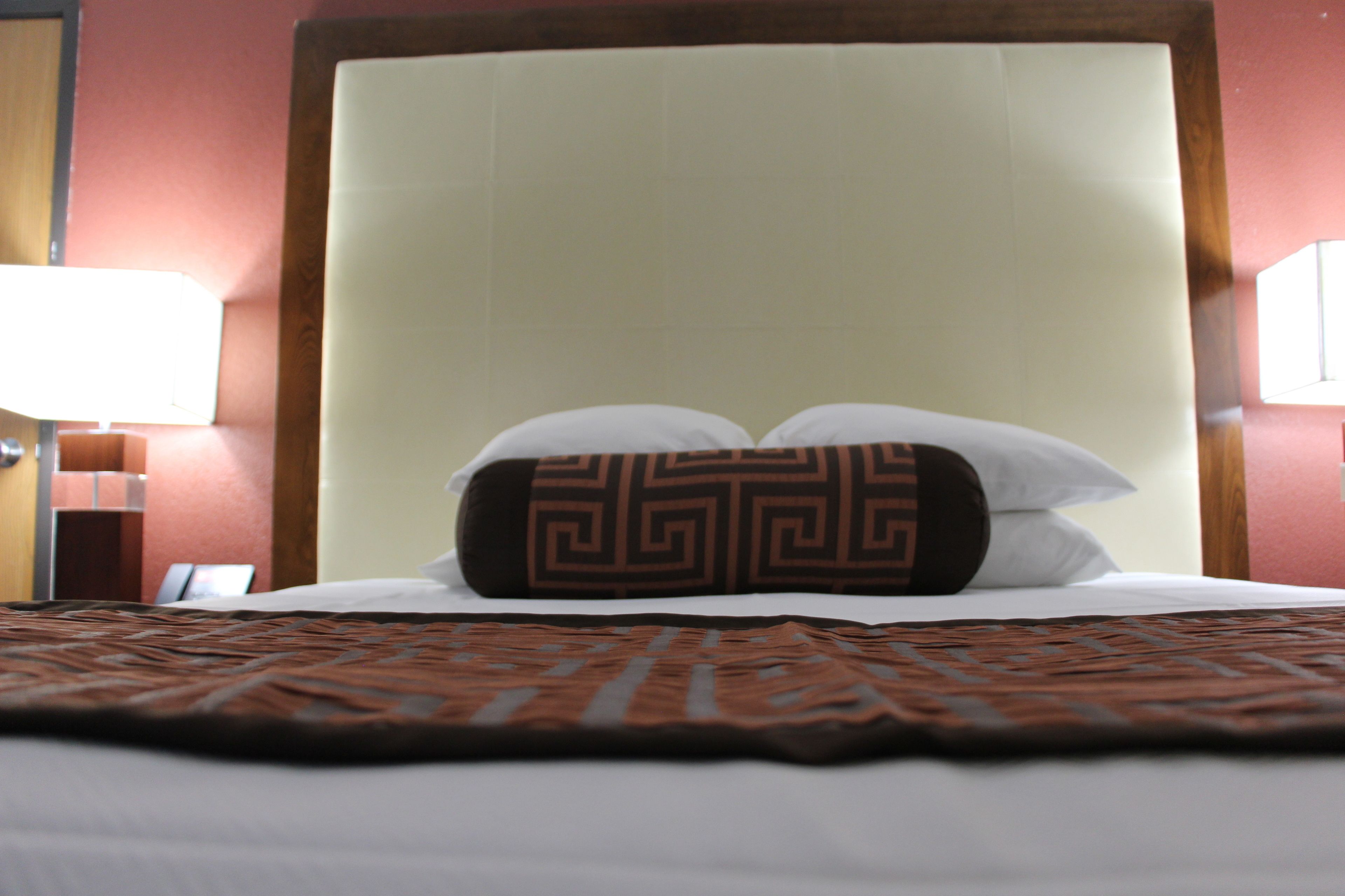 A hotel room with a large bed, a headboard, and a patterned bedspread.