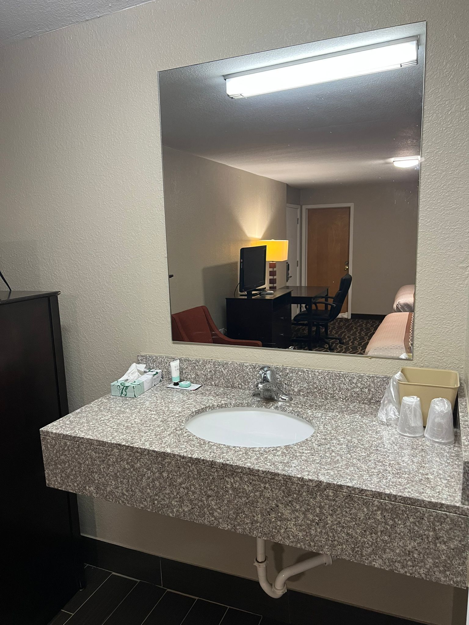 A bathroom with a granite countertop, a sink, a mirror, and a toilet.