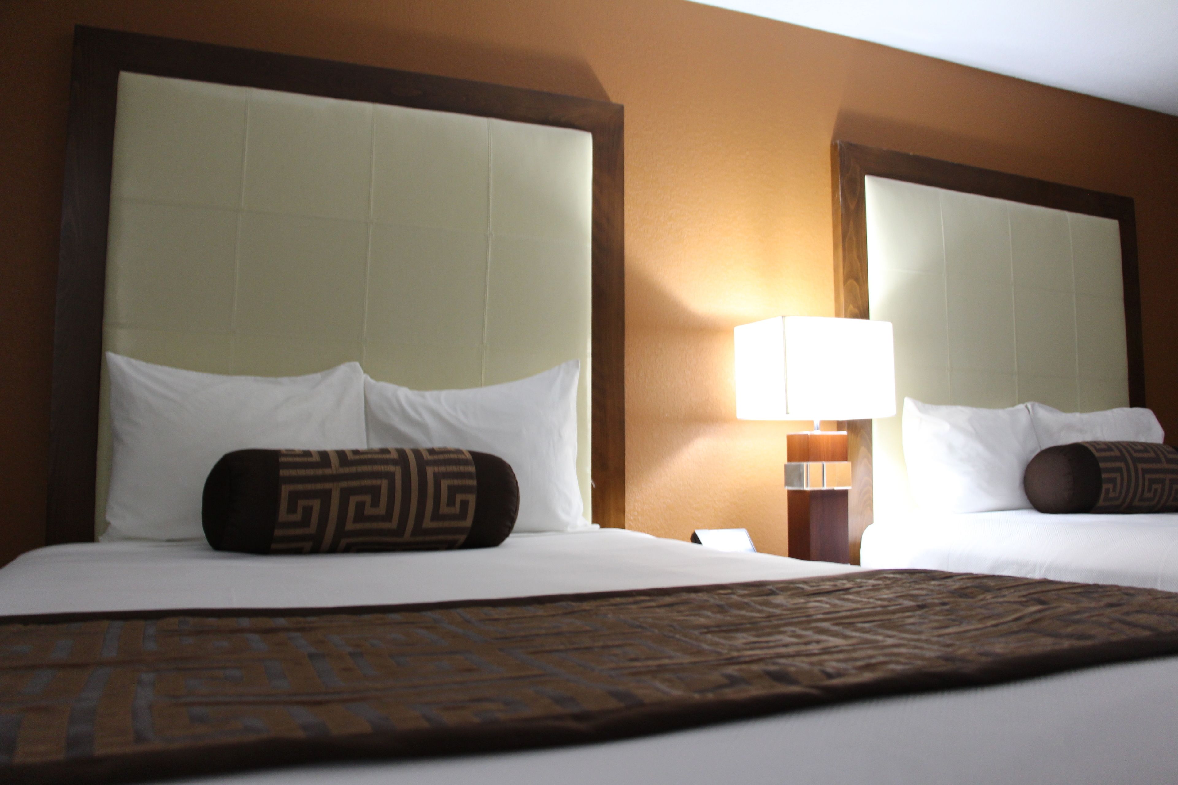 Two hotel beds with headboards, a lamp, and a patterned bedspread.