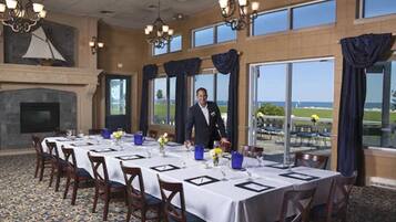 A formal dining room with a long table set for a meal, large windows with a view, and a fireplace.