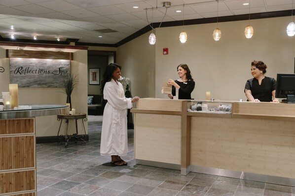 A reception area with a reception desk, a wall-mounted sign reading "Reflections Spa," and a small side table with candles.
