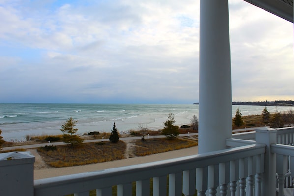 Une vue sur la plage depuis une véranda dotée d’une balustrade, avec les vagues de l’océan et un ciel nuageux.