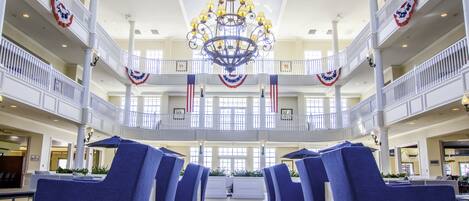A spacious lobby with a central chandelier, multiple levels with balconies, and rows of blue chairs.