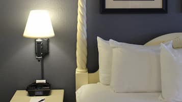 Una habitación de hotel con una cama, una lámpara de noche, una mesita de noche con un teléfono, un cuadro en la pared y un adorno decorativo con forma de cuerda.