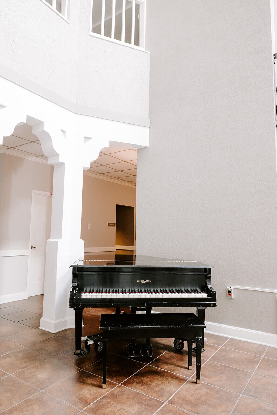 A black upright piano in a spacious room with a high ceiling and a white column structure.
