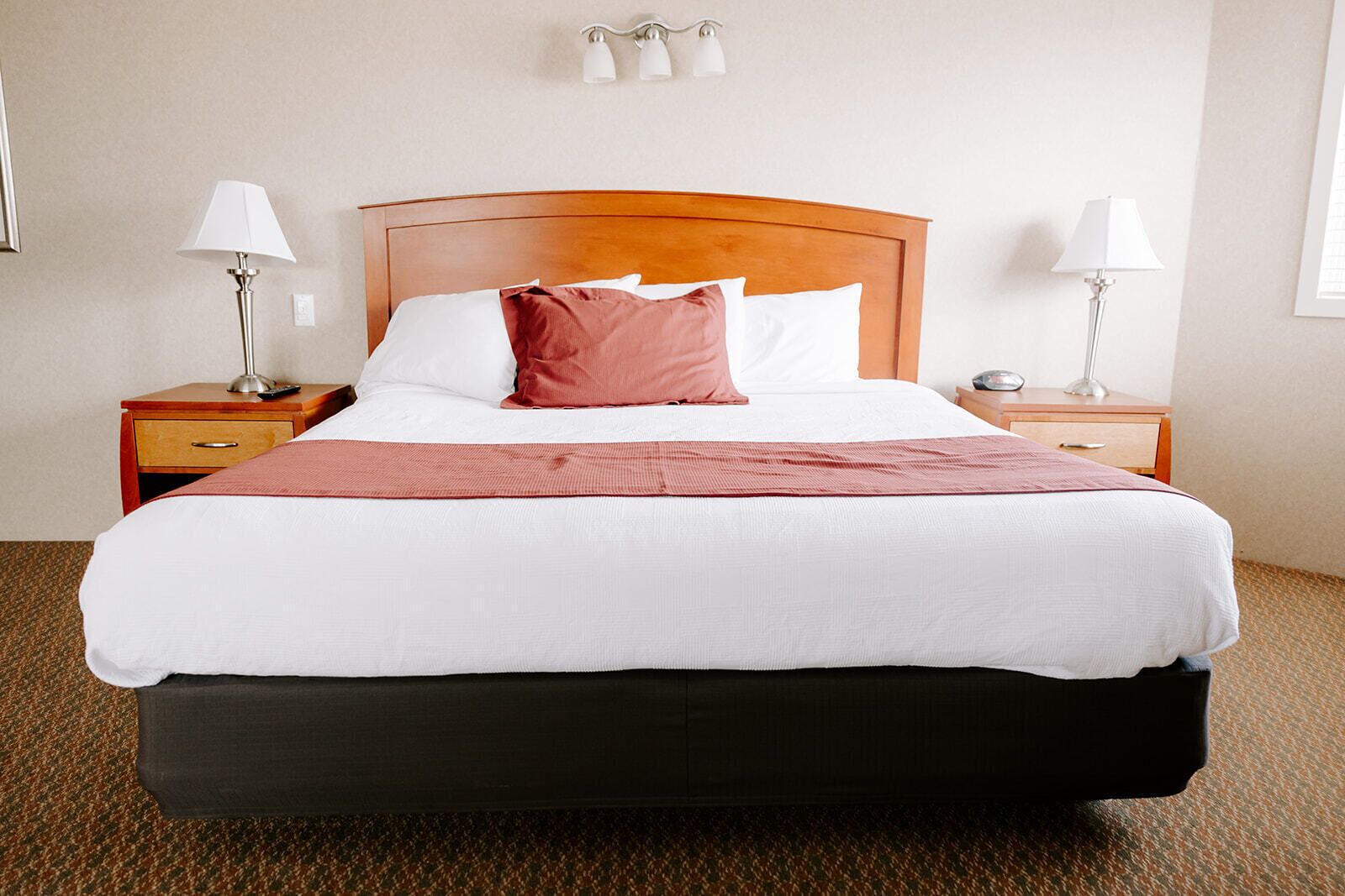 A hotel room with a large bed, two bedside tables with lamps, a wooden headboard, and a carpeted floor.