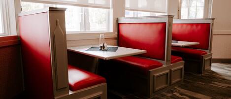 A restaurant with booths and tables, featuring red seating and large windows.