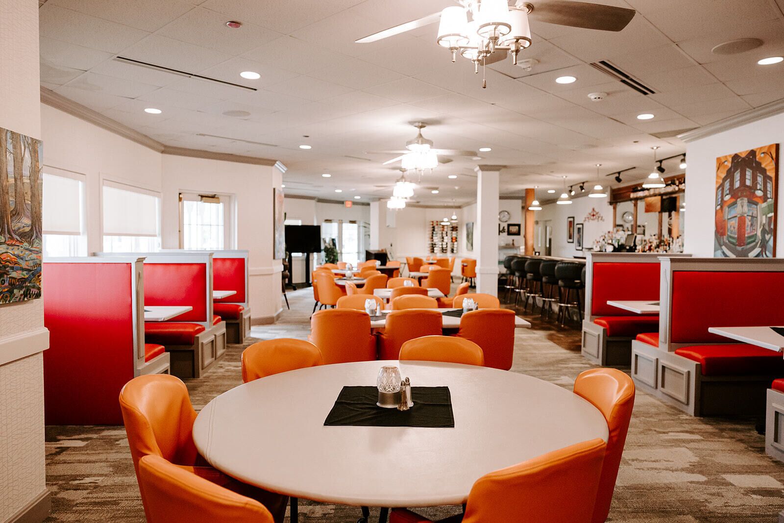 A restaurant with red booths and orange chairs, featuring a round table with a glass and napkin.