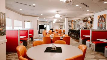 A restaurant with red booths and orange chairs, featuring a round table with a glass and napkin.