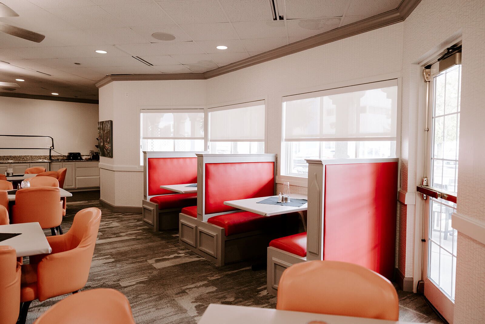 A restaurant with red booths and orange chairs, large windows, and a carpeted floor.