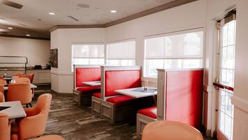 A restaurant with red booths and orange chairs, large windows, and a carpeted floor.