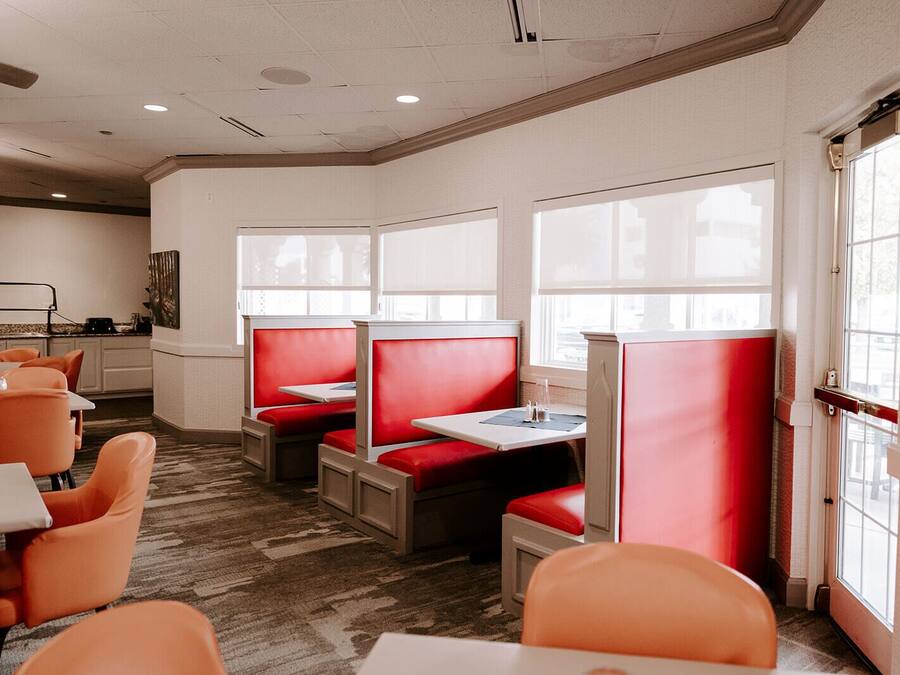 A restaurant with red booths and orange chairs, large windows, and a carpeted floor.