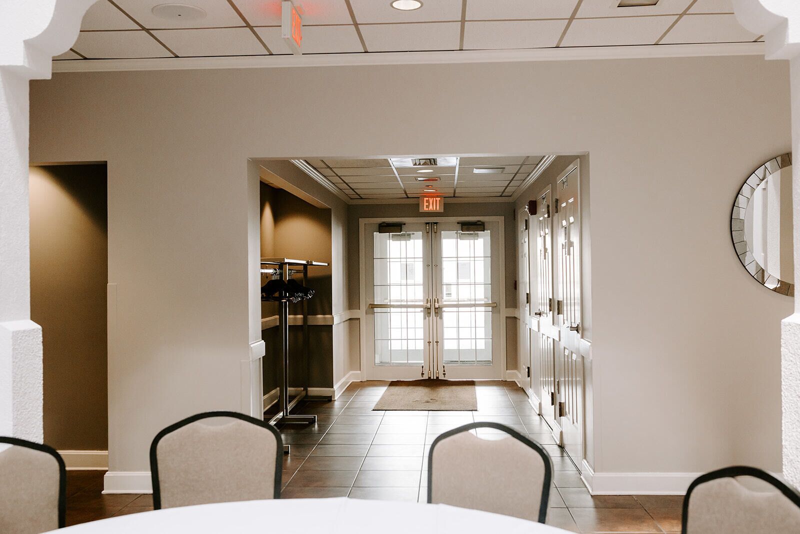 A hotel lobby with a conference table, chairs, a coat rack, and a door with an exit sign.