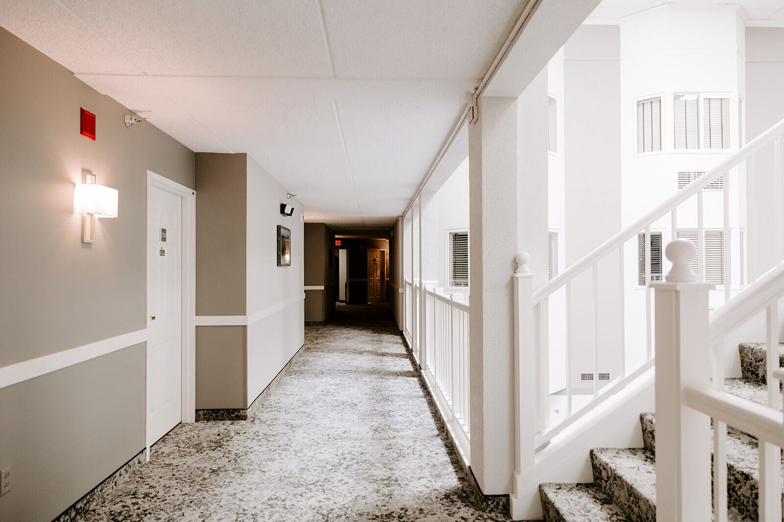 Um corredor de hotel com piso de mármore, paredes brancas e escada com guarda-corpo branco.