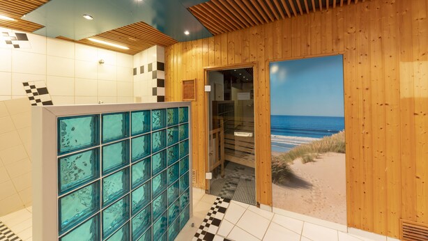 A bathroom with a glass shower enclosure, wooden walls, and a view of the beach. - Hotel Lechnerhof (Unterfoehring)