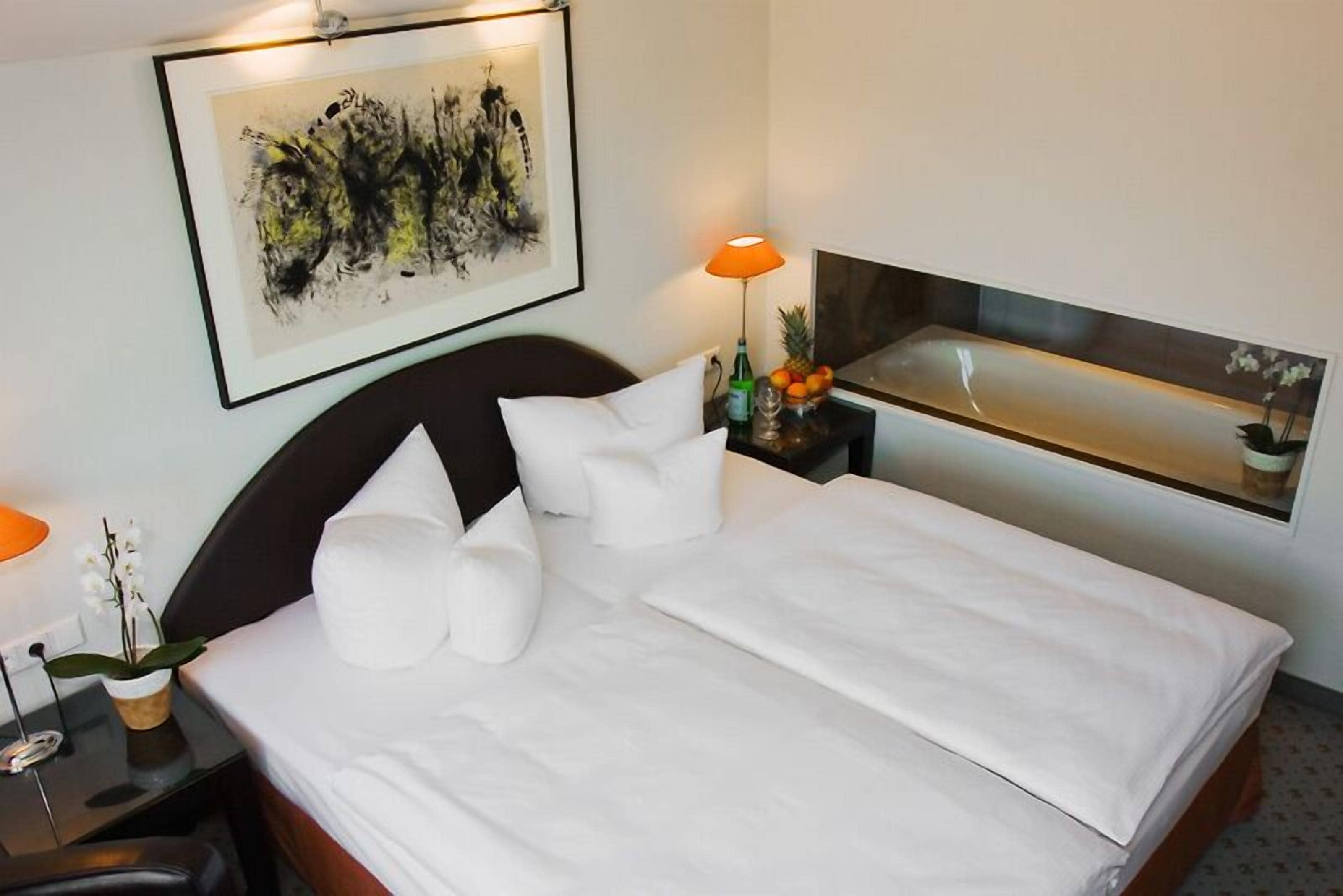 Una cama bien hecha con ropa blanca, un cabecero negro y un cuadro abstracto enmarcado encima.