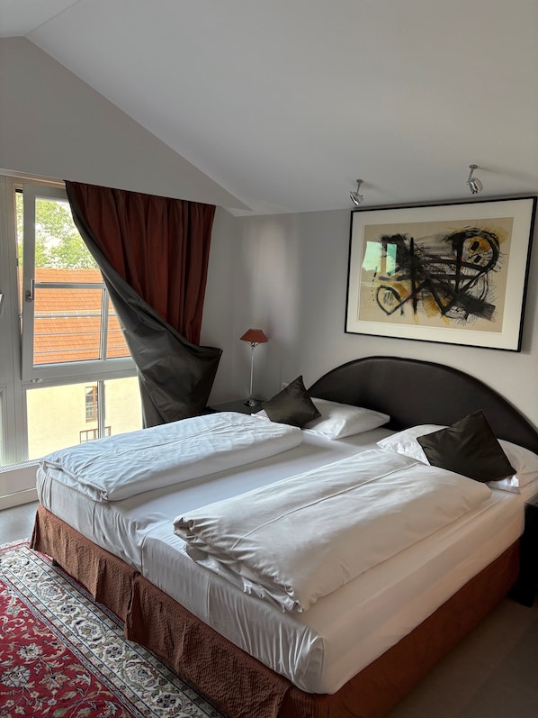 A double bed with white linens, a dark headboard, and a red patterned rug. - Hotel Lechnerhof (Unterfoehring)