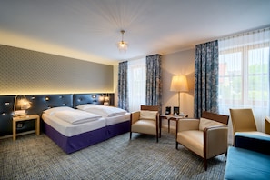 Relax in this stylish room with a large bed, armchairs, and sofa, offering a view of the outside through large windows.