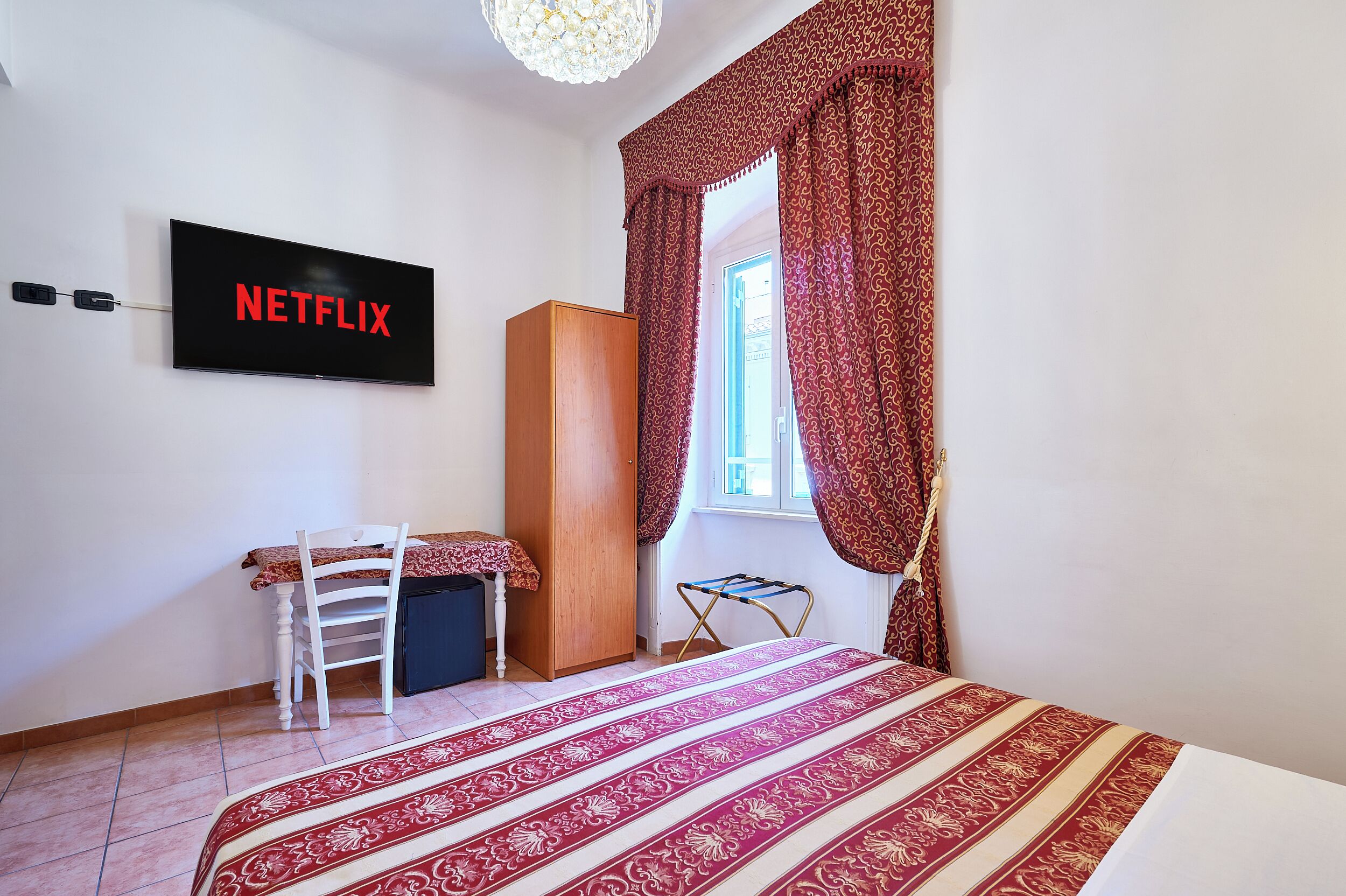 Una camera da letto con un letto, una scrivania, un armadio e una TV a parete con il logo Netflix.