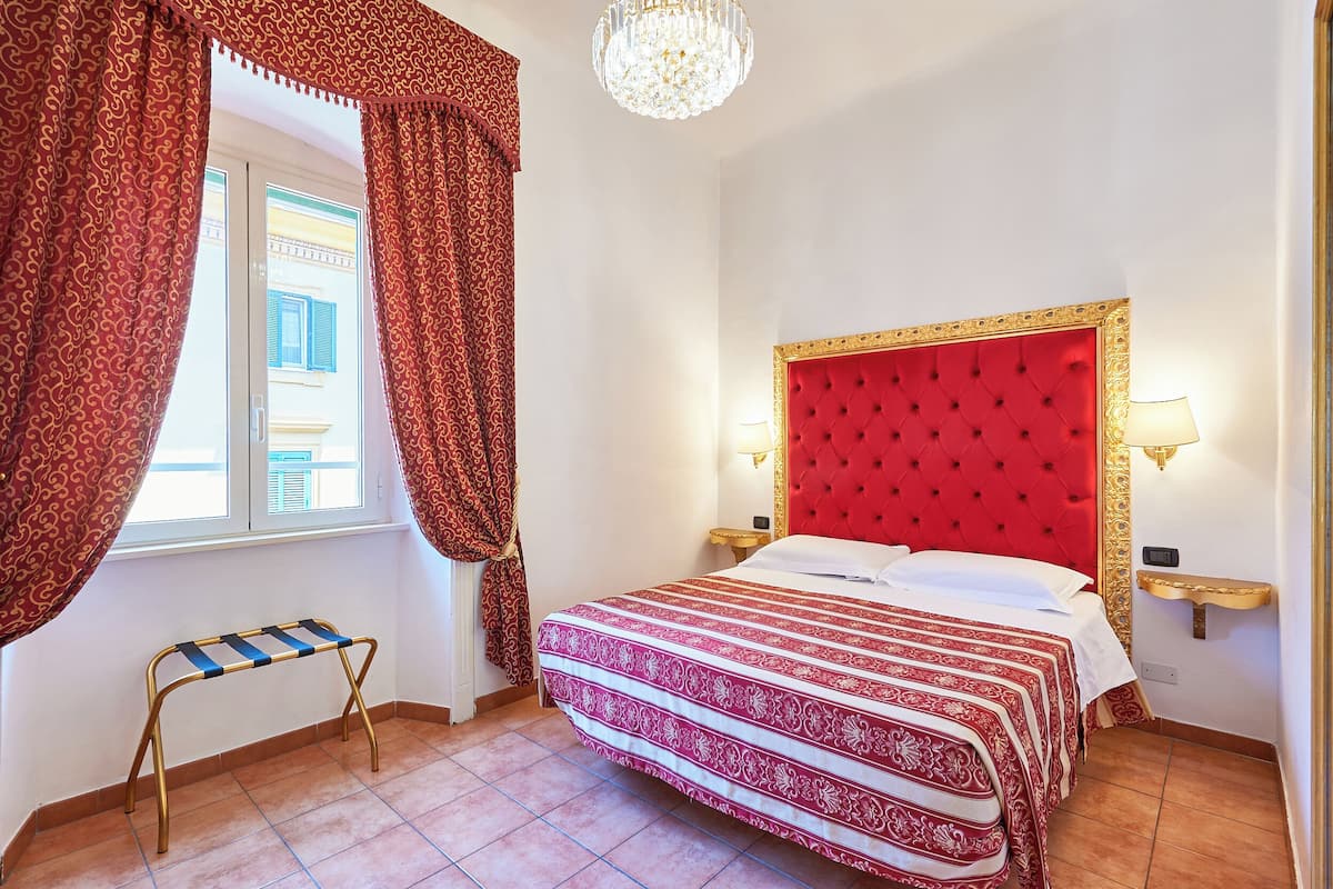 Une chambre d’hôtel avec un lit, des rideaux, un lustre et une petite table.