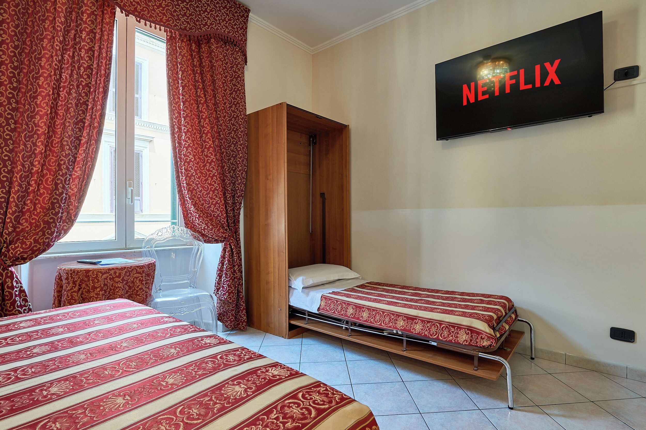 A hotel room with two beds, a TV mounted on the wall, and a window with curtains.