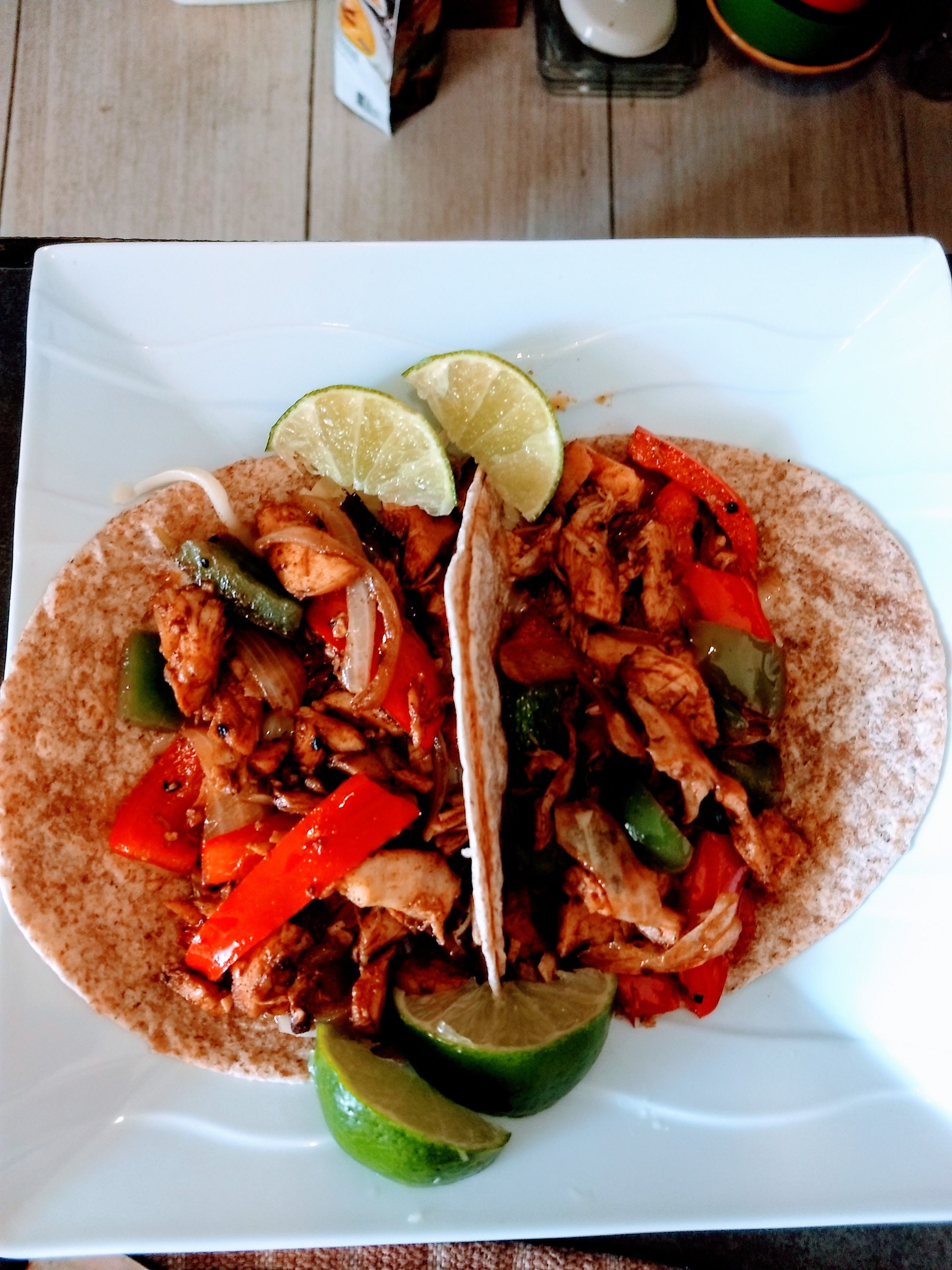 Un plato de comida con tortillas, pollo, pimientos y gajos de lima.