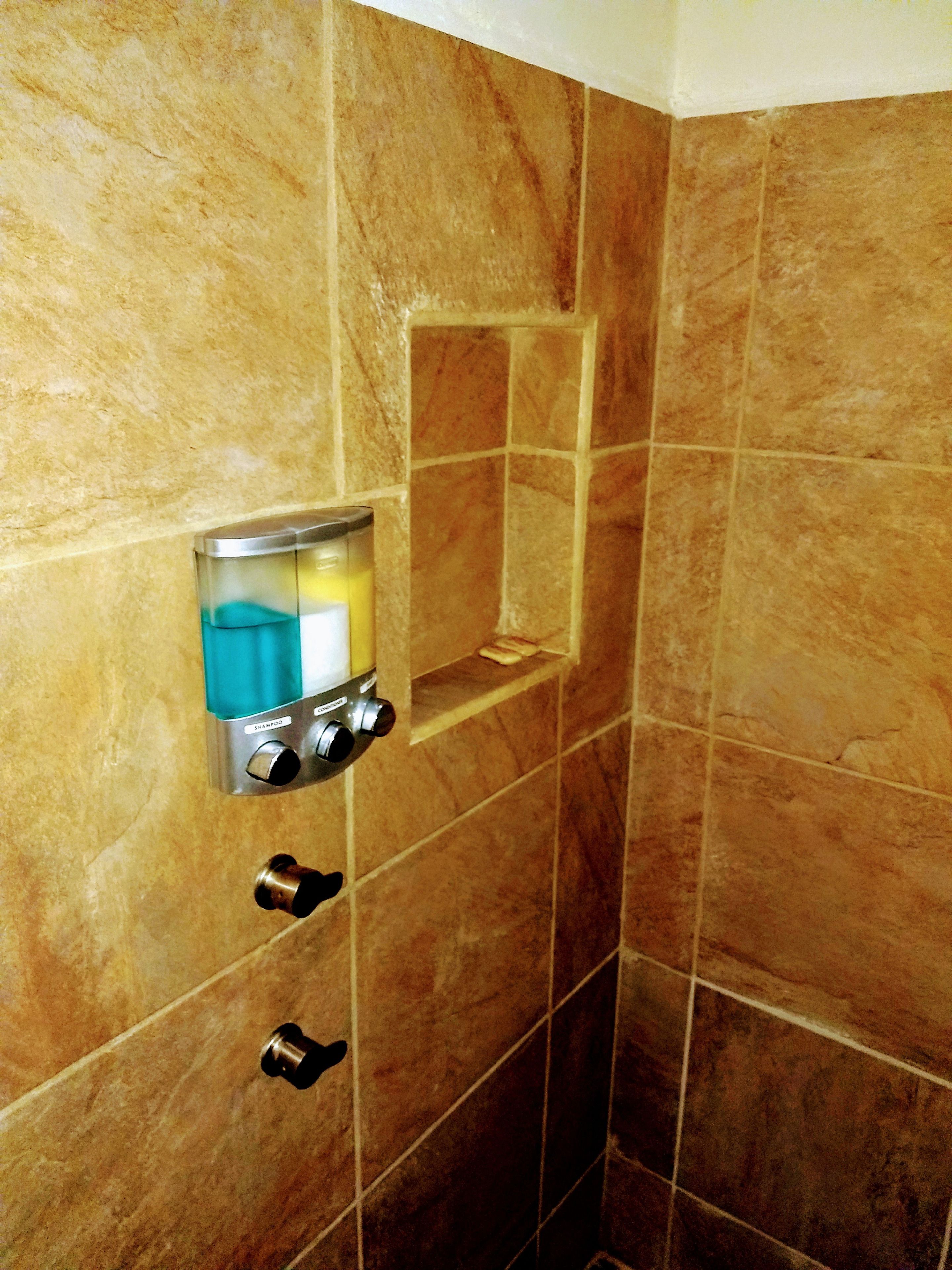 A bathroom with a shower area, a built-in shampoo dispenser, and a soap dish.