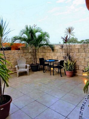 Eine Terrasse im Freien mit einer Steinwand, einem weißen Stuhl, einem Tisch und mehreren Kübelpflanzen.