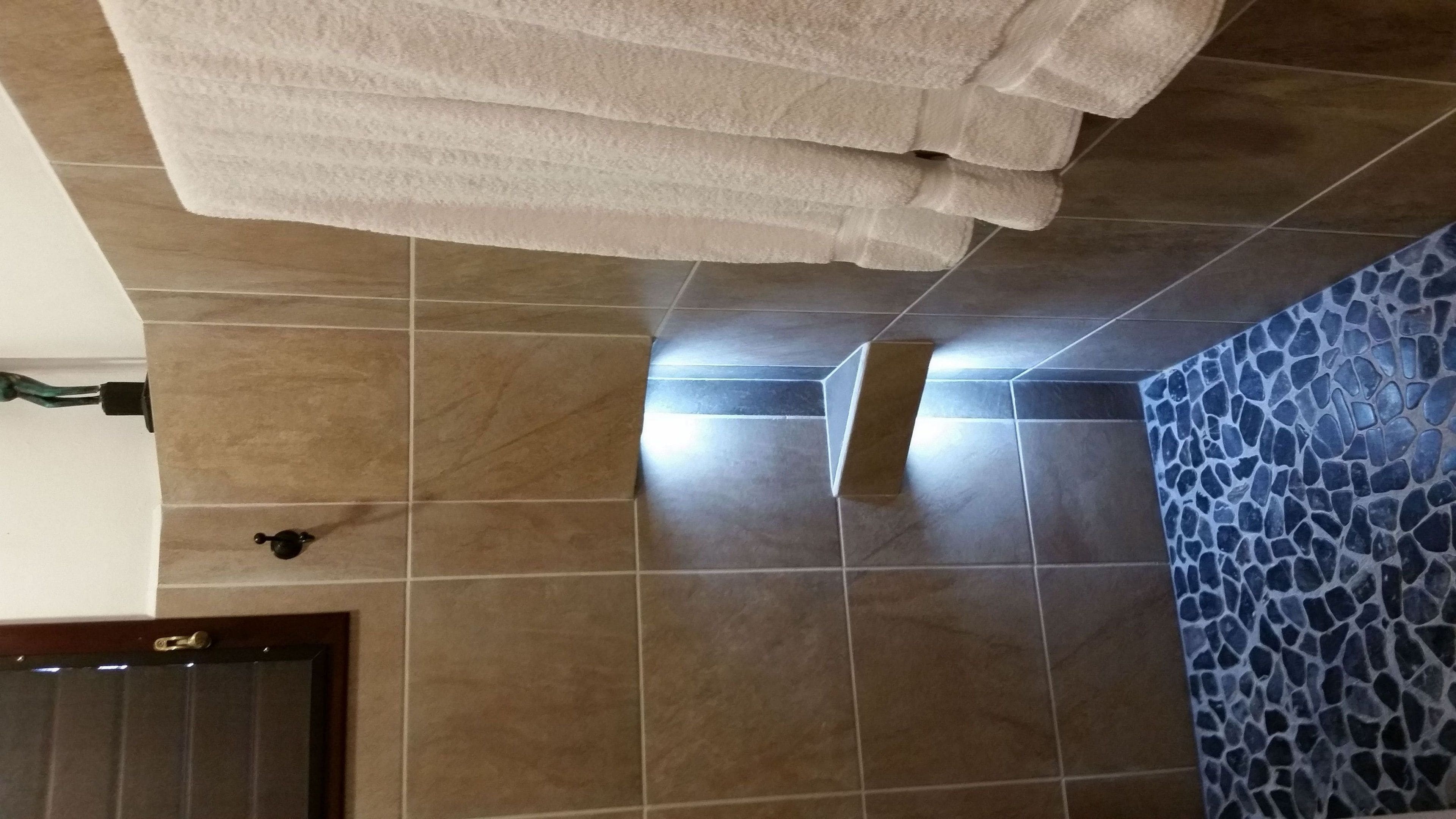 Un baño con baldosas color beige, un muro de mosaico azul y un perchero.